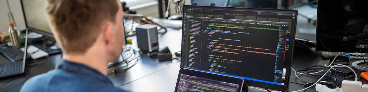 Programmer writing code on a laptop with an external monitor